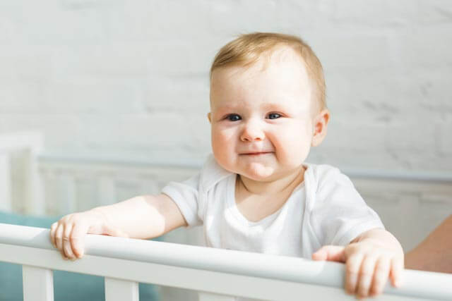 Baby steht in einem Gitterbett